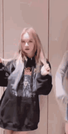 a woman in a black hoodie is standing in front of a wall and dancing .