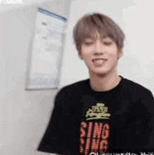 a young man wearing a black t-shirt that says sing on it is smiling .