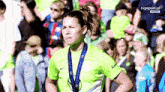 a woman in a green shirt with a medal around her neck stands in front of a tv screen that says tvpsport.pl on it