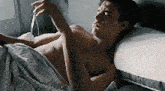 a shirtless man is laying on a bed holding a bottle of water