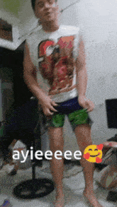 a man wearing shorts and a shirt that says ayieeee is standing in front of a fan