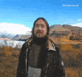 a man with long hair and a beard stands in front of mountains and a lake with pixverse.ai written in the corner