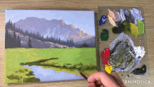 a painting of a mountain landscape is being painted on a canvas next to a palette of paint