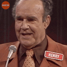 a man wearing a name tag that says henry stands in front of a microphone