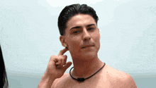a shirtless man wearing a black necklace is covering his ear with his hand