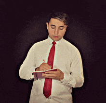 a man in a white shirt and red tie is writing on a notepad