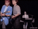 a man is playing a guitar while another man plays a keyboard on a stage .