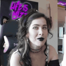 a woman wearing black lipstick is sitting in front of a sign that says life is wiz