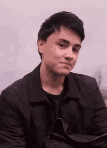 a young man wearing a black jacket and a black shirt is sitting at a table .
