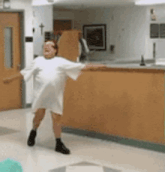 a woman in a white hospital gown is dancing in a hospital hallway .