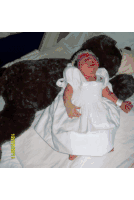 a baby in a white dress is laying next to a brown teddy bear on a bed