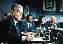 a man in a suit sits at a table in front of a microphone