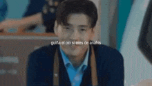 a man in a blue shirt and black jacket is smiling in a blurry photo with spanish text .