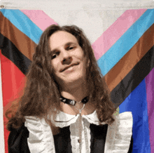 a man with long hair wearing a maid outfit stands in front of a rainbow flag