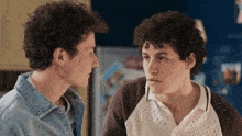 two men with curly hair are looking at each other in front of a blue refrigerator