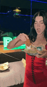 a woman in a red dress holds a plate of food in front of a green sign that says p.