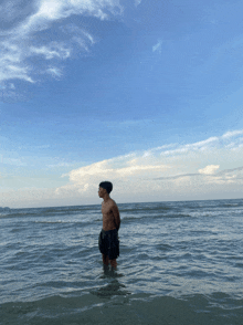a shirtless man is standing in the ocean looking up at the sky