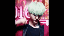 a man with green hair and a red jacket is standing in front of a neon sign .