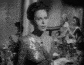a black and white photo of a woman standing in front of a table