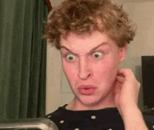 a young man with curly hair is making a funny face while looking at himself in the mirror .