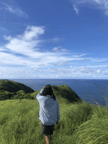 a person standing on top of a grassy hill looking at the ocean