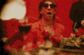 a man in a red suit and sunglasses is sitting in front of red flowers