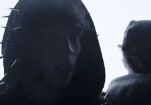 a man wearing a black hoodie with spikes on it looks at the camera