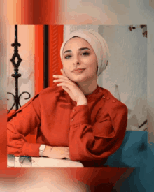 a woman wearing a head scarf and a red shirt has her hand on her chin