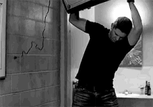 a black and white photo of a man holding a box over his head .