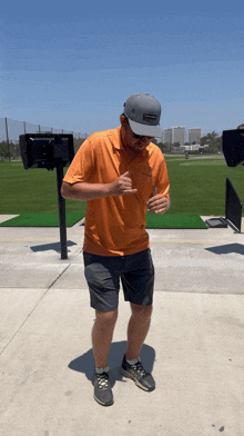 a man wearing an orange shirt and gray shorts is standing in front of a golf course