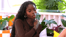 a woman in a brown shirt is sitting on a couch in front of plants