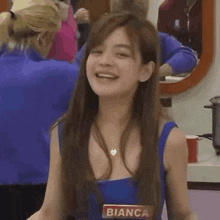a woman in a blue tank top is smiling in front of a mirror .