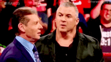 two men are standing next to each other in front of a crowd and talking .