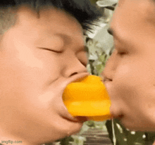 a man is kissing another man on the cheek while eating a mango .