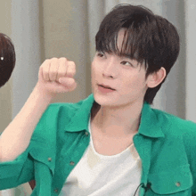 a young man wearing a green shirt and a white shirt is making a fist .