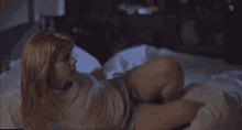 a woman in a white tank top is laying on a bed in a dark room
