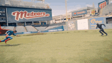 a man in a superman costume is running on a baseball field in front of a sign for the meteors