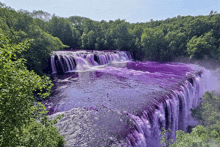 a purple waterfall is surrounded by trees and a blue sky