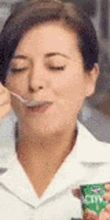 a woman is eating yogurt with a spoon from a green cup
