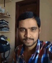 a man in a plaid shirt is taking a selfie in a room