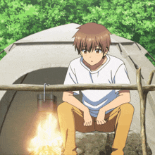 a boy is sitting in front of a tent with a campfire in the background