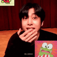 a young man is covering his mouth with his hand next to a frog cartoon .