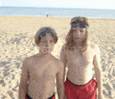 two young boys standing on a sandy beach wearing goggles and red shorts