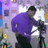 a man in a purple shirt stands in front of a camera