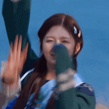 a girl is covering her nose with her hand while wearing a green jacket