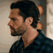 a man with a beard wearing a plaid shirt looks to the side