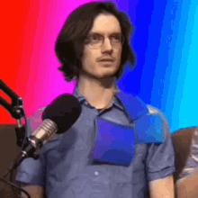 a man wearing glasses and a blue shirt is standing in front of a microphone with a colorful background .