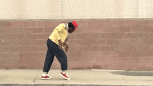 a man wearing a red hat and a yellow jacket is walking down the sidewalk .