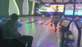 a man sits in a bowling alley while a woman throws a ball