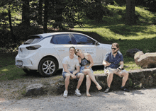 three people sitting on a rock in front of a white car with a sticker that says renault